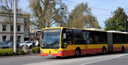 Ulica, po której jedzie czerwono-pomarańczowy autobus komunikacji miejskiej. Nad jego przednią szybą wyświetla się napis: 710 Konstancin-Jeziorna.