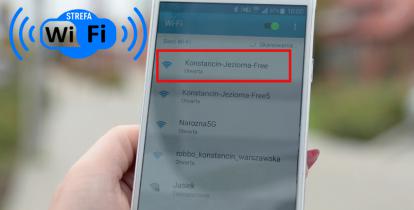 Ręka trzymająca smartfona, na ekranie lista dostępnych sieci wifi, czerwoną ramką zaznaczona sieć o nazwie Konstancin-Jeziorna Free, w górnym lewym roku napis strefa wifi.