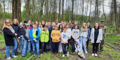 Grupa młodzieży stojąca w grupie razem z dwójką nauczycieli, pozujący do zdjęcia na tle podmokłego lasu.