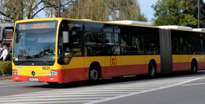 Ulica, po której jedzie czerwono-pomarańczowy autobus komunikacji miejskiej. Nad jego przednią szybą wyświetla się napis: 710.