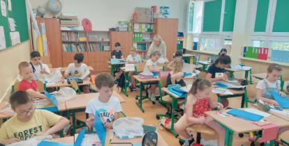 dzieci siedzące w klasie w szkolnych ławkach