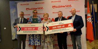 Pięć osób, w tym dwie kobiety, stoją obok siebie i trzymają w rękach dwa duże czeki z kwotą 20 tys. zł i 200 tys. zł. 