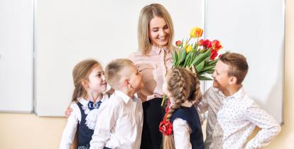 Sala lekcyjna. Czterech uczniów w wieku 10 lat składa życzenia i bukiet swojemu nauczycielowi.