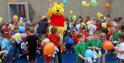 Pluszowa maskotka w towarzystwie dzieci bawiących się balonami.
