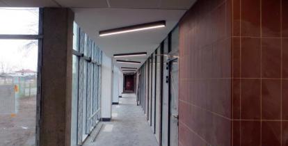 Długi korytarz w budynku szkoły, z lewej wysokie okna.