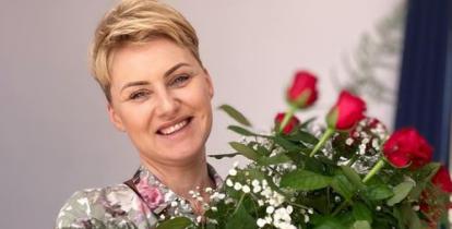 Młoda kobieta z krótkimi blond włosami i bukietem czerwonych róz w dłoniach.