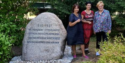 Trzy kobiety stoją przy głazie pamiątkowym w parku.