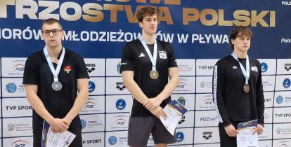 Troje młodych mężczyzn stojących na podium. Na szyjach mają medale.