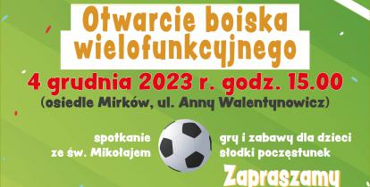 Grafika przedstawia plakat informujący o otwarciu boiska wielofunkcyjnego. Tłem jest zielona murawa, a w pierwszym planie znajdują się nożyce przecinające czerwoną wstęgę.