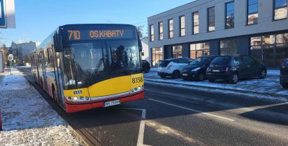 Ulica, po której jedzie czerwono-pomarańczowy autobus komunikacji miejskiej.