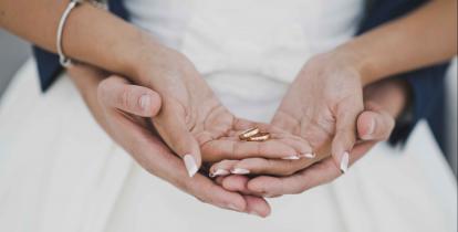 Nowożeńcy: dłonie meżczyzny podtrzymują od spodu dłonie kobiety. Kobieta w dłoniach trzeba obrączki.