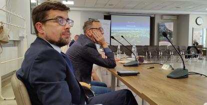 Mężczyzna w garniturze i w okularach siedzi za stołem w sali konferencyjnej