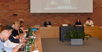 Grupa osób siedzi przy stołach w sali posiedzeń.