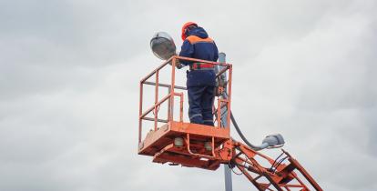 Elektryk naprawiający latarnię uliczną na wysokości.