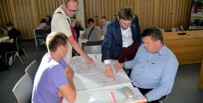 Kilka osób patrzy na mapę tras autobusowych leżącą na stoliku