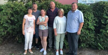 grupka osób stoi na tle krzaków 
