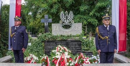 Dwóch strażników miejskich pełni wartę przy nagrobku na cmentarzu.