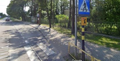 Fragment ulicy z chodnikiem, w tle przystanek autobusowy