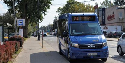 Niebieski autobus stoi na przystanku, w tle ulica z samochodami.