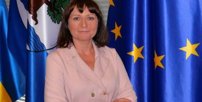 Kobieta z założonymi rękoma na tle flag Konstancina-Jeziorny i Unii Europejskiej.