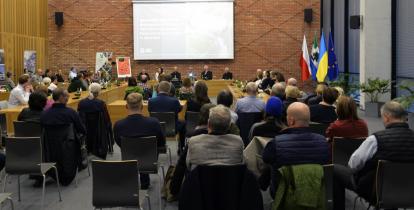 Sala posiedzeń wypełniona osobami siedzącymi na krzesełkach