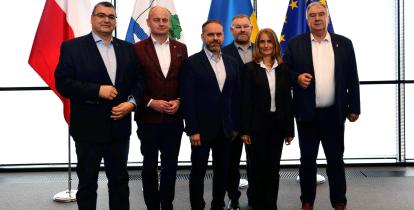 Grupa osób ubrana w garnitury na tle flag.