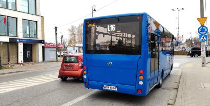 Niebieski autobus stoi na przystanku, w tle ulica z samochodami.