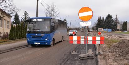 Niebieski autobus komunikacji miejskiej przejeżdżający przez drogę w trakcie remontu, oznaczoną zakazem wjazdu z wyłączeniem pojazdów budowy i mieszkańców. Po prawej stronie widać barierki oraz oznaczenia ostrzegawcze, a w tle maszyny budowlane i sprzęt wykorzystywany podczas prac.
