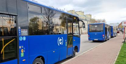 Trzy niebieskie autobusy miejskie stoją zaparkowane na przystanku wzdłuż chodnika przy ulicy.