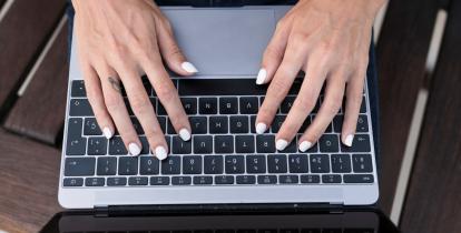 Kobieta z pomalowanymi na biało paznokciami pracuje na laptopie, trzymając dłonie na klawiaturze.