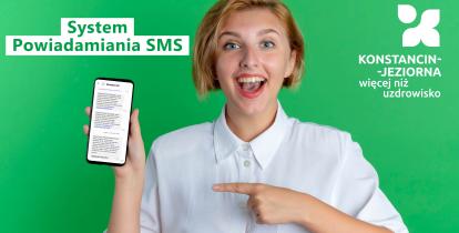 Młoda kobieta z szerokim uśmiechem trzyma w dłoni smartfon z wiadomościami SMS, na zielonym tle z napisami promującymi system powiadamiania SMS dla Konstancina-Jeziorny.