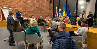 Grupa ludzi siedzi obok siebie z zeszytami i długopisami w ręku