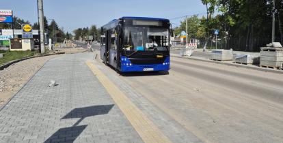Niebieski autobus jadący ulicą w pobliżu sklepu Lidl, na tle trwających prac drogowych i świeżo ułożonego chodnika.