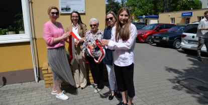 Pięć kobiet, w tym uczennica i seniorka, trzyma wstęgę podczas uroczystego odsłonięcia tablicy pamiątkowej na budynku przy ul. Jana Sobieskiego 6 w Konstancinie-Jeziornie.