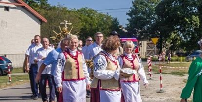 Kolorowy korowód dożynkowy z udziałem mieszkańców w tradycyjnych strojach ludowych i dziewcząt niosących wieniec z kłosów zbóż podczas święta plonów.