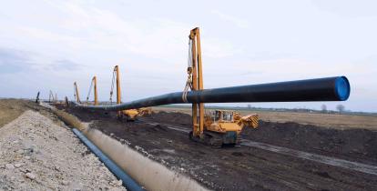 Ciężkie maszyny budowlane przenoszą i umieszczają rury gazociągowe w ziemi.