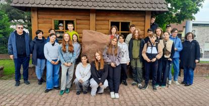 wycieczka szkolna, przed drewnianym budynkiem i kamiennym pomnikiem