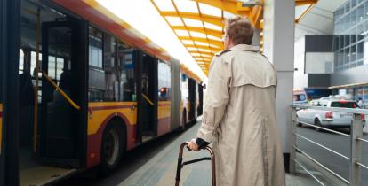 Kobieta stoi na przystanku autobusowym i chce wsiąść do pojazdu.