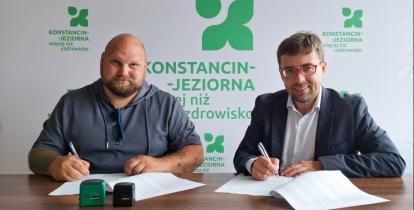 Dwóch mężczyzn siedzi przy biurku i podpisuje dokumenty.