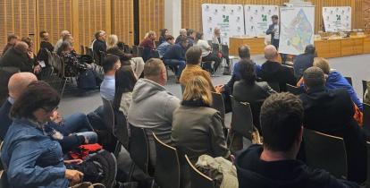 Grupa ludzi siedzi na krzesłach w sali konferencyjnej i słuch prezentacji.