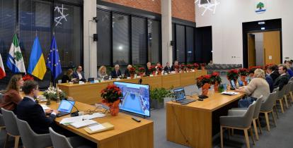 Grupa osób siedzi za stołami na sali posiedzeń.