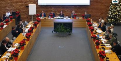 Sala obrad podczas sesji budżetowej – radni zasiadają przy długich stołach ustawionych w podkowę, a w tle widoczna jest świąteczna dekoracja z choinką i poinsecjami.