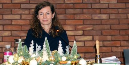 Uśmiechnięta kobieta za stołem prezydialnym, na tle ściany z czerwonej cegły.