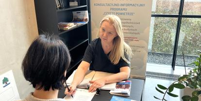 Dwie kobiety siedzą naprzeciwko siebie. Jedna z nich pokazuje drugiej dokument.