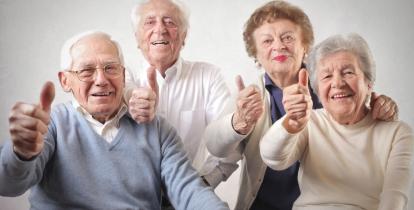 Czworo uśmiechniętych seniorów siedzi obok siebie i pokazuje uniesione kciuki na znak zadowolenia.