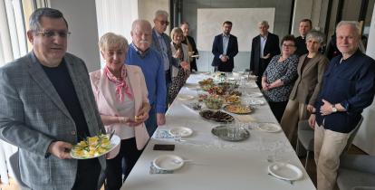 Burmistrz Michał Wiśniewski i przewodniczący Rady Seniorów Wojciech Guszkowski stoją przy stole z grupą seniorów podczas spotkania przedświątecznego w urzędzie gminy.