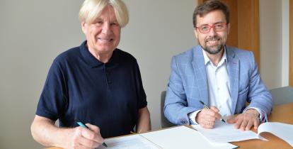 Dwóch mężczyzn siedzi przy stole i podpisuje dokumenty podczas zawarcia porozumienia dotyczącego współpracy Muzeum Villa la Fleur z Konstancińską Kartą Mieszkańca.