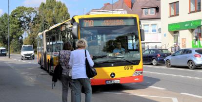 Żółto-czerwony autobus linii 710 zatrzymuje się na przystanku w centrum Konstancina-Jeziorny, gdzie na chodniku czekają pasażerowie.