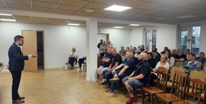 Grupa osób w sali świetlicowej słucha wystąpienia burmistrza