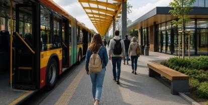 Wizualizacja nowoczesnego węzła przesiadkowego z autobusem, budynkiem poczekalni oraz pasażerami korzystającymi z infrastruktury transportu publicznego.
